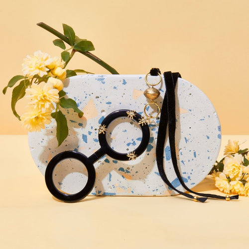 Colgante gafas Hormigas, realizado en acetato color negro con hormigas metálicas doradas y collar de terciopelo negro con fornituras  y abalorios dorados. El colgante tiene una bisagra que hace que se pueda desplegar y transformar en gafas de lectura.