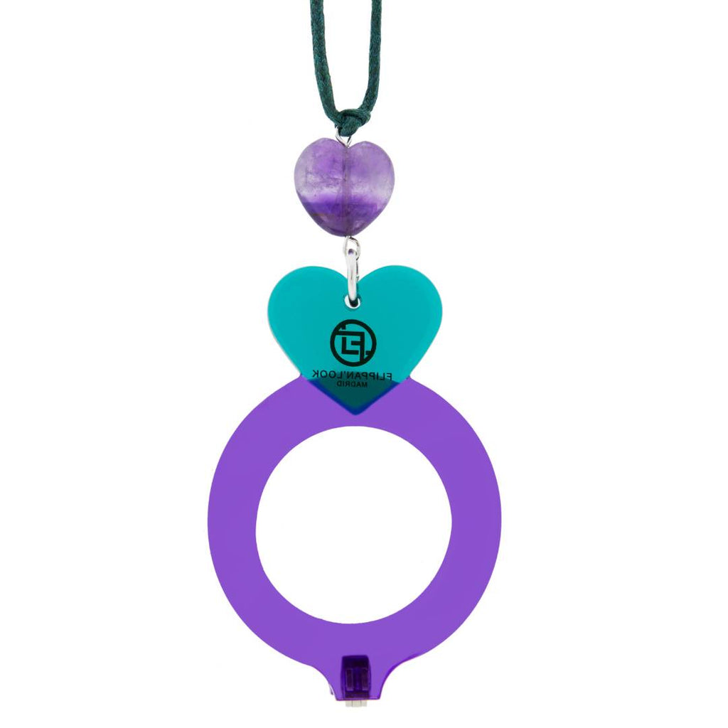Colgante de acetato en morado y verde tranparente, con una bisagra que hace que se transforme en gafas de lectura. Collar hecho en cordón de algodón verde, abalorio de piedras en forma de corazón y fornituras plateadas.