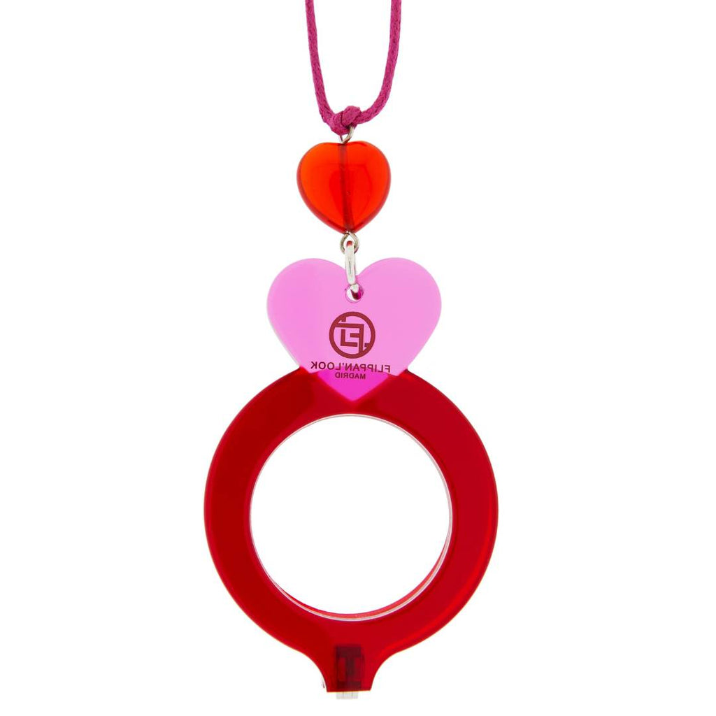 Colgante de acetato en rojo y rosa tranparente, con una bisagra que hace que se transforme en gafas de lectura. Collar hecho en cordón de algodón fucsia, abalorio de cristal en forma de corazón y fornituras plateadas.
