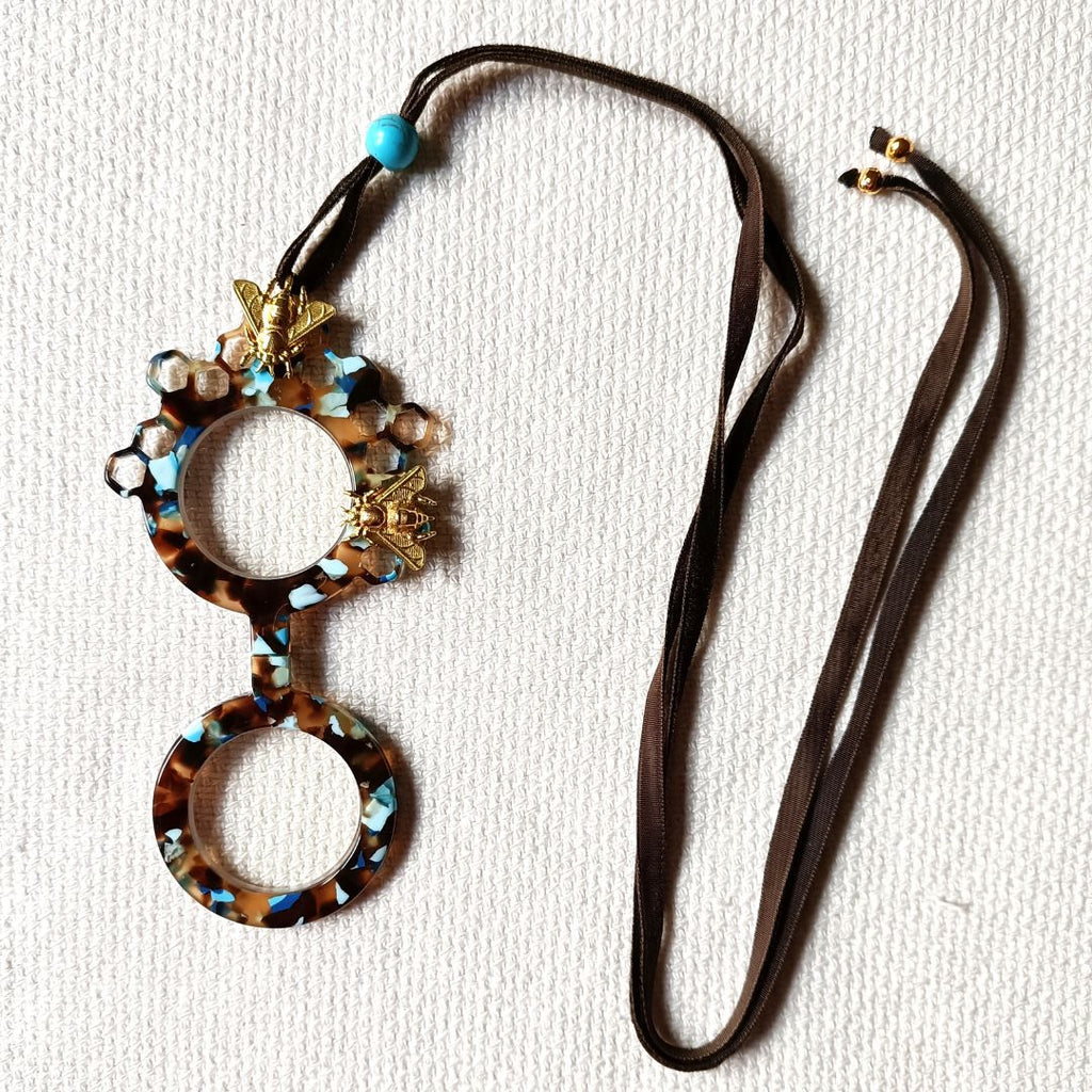 Medallón-gafas de acetato en tonos carey y turquesas, realizado en acetato y con abejas metálicas en color dorad. Rematado con collar de terciopelo con abalorio en color turquesa.Transformable en gafas de lectura.