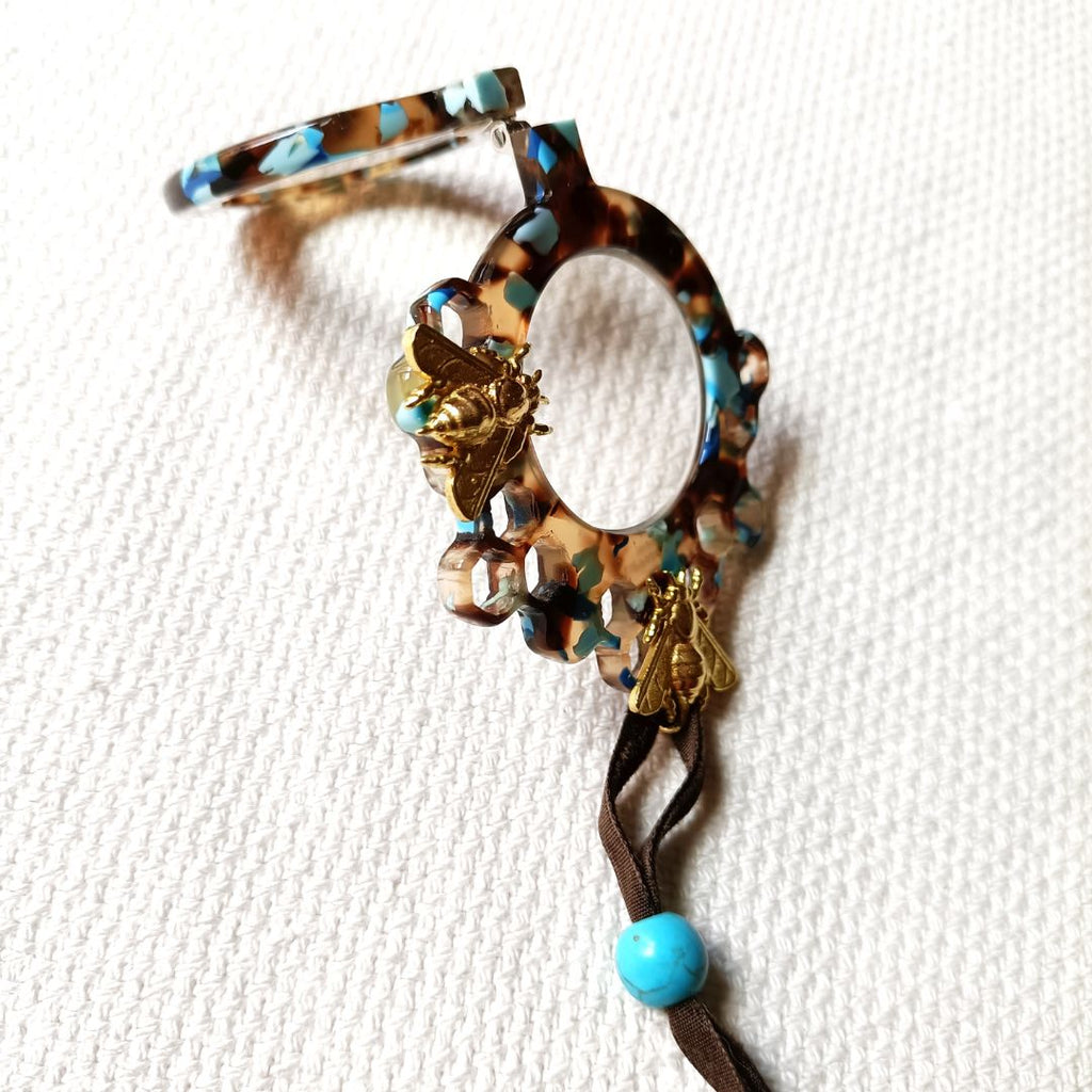 Medallón-gafas de acetato en tonos carey y turquesas, realizado en acetato y con abejas metálicas en color dorad. Rematado con collar de terciopelo con abalorio en color turquesa.Transformable en gafas de lectura.