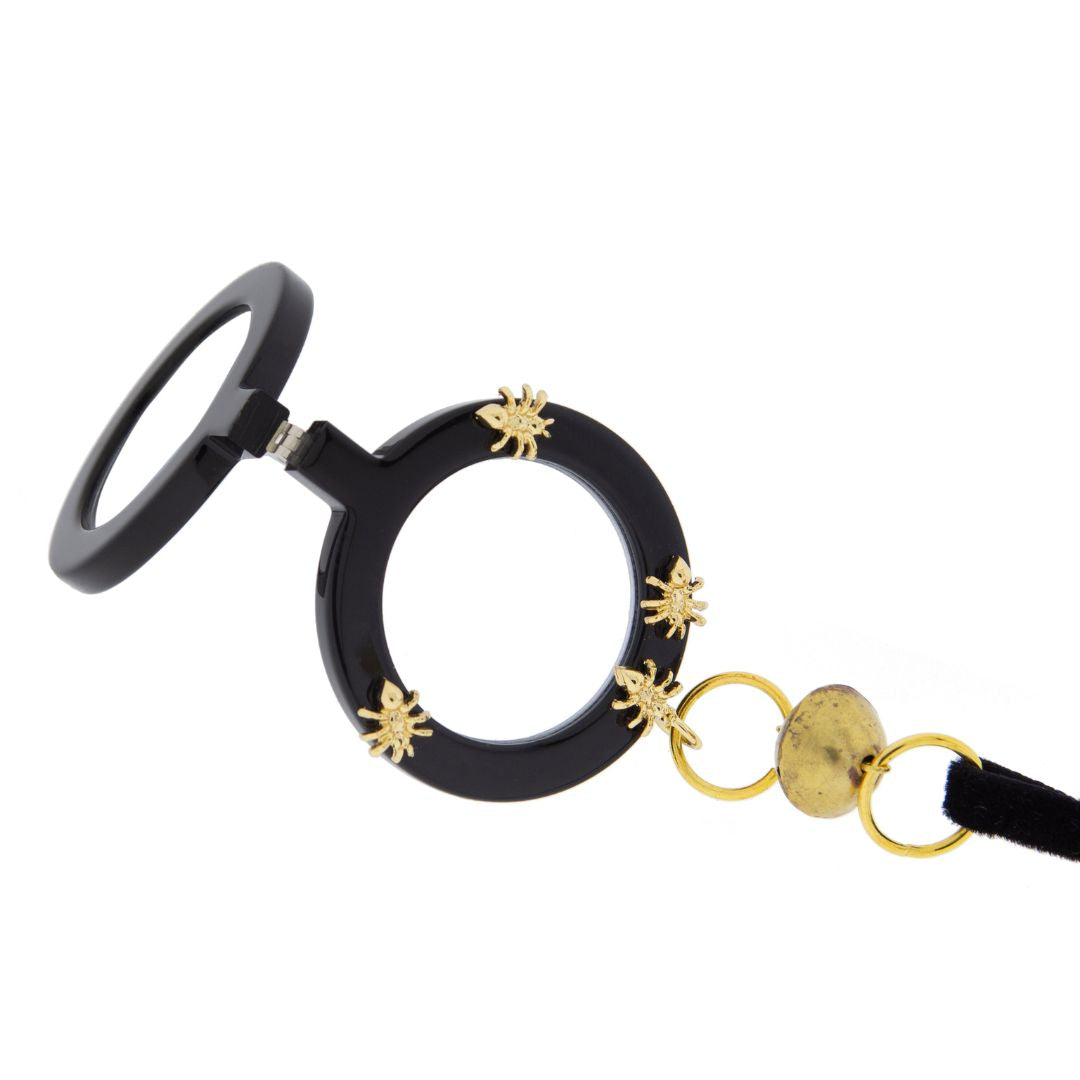 Colgante gafas Hormigas, realizado en acetato color negro con hormigas metálicas doradas y collar de terciopelo negro con fornituras  y abalorios dorados. El colgante tiene una bisagra que hace que se pueda desplegar y transformar en gafas de lectura.