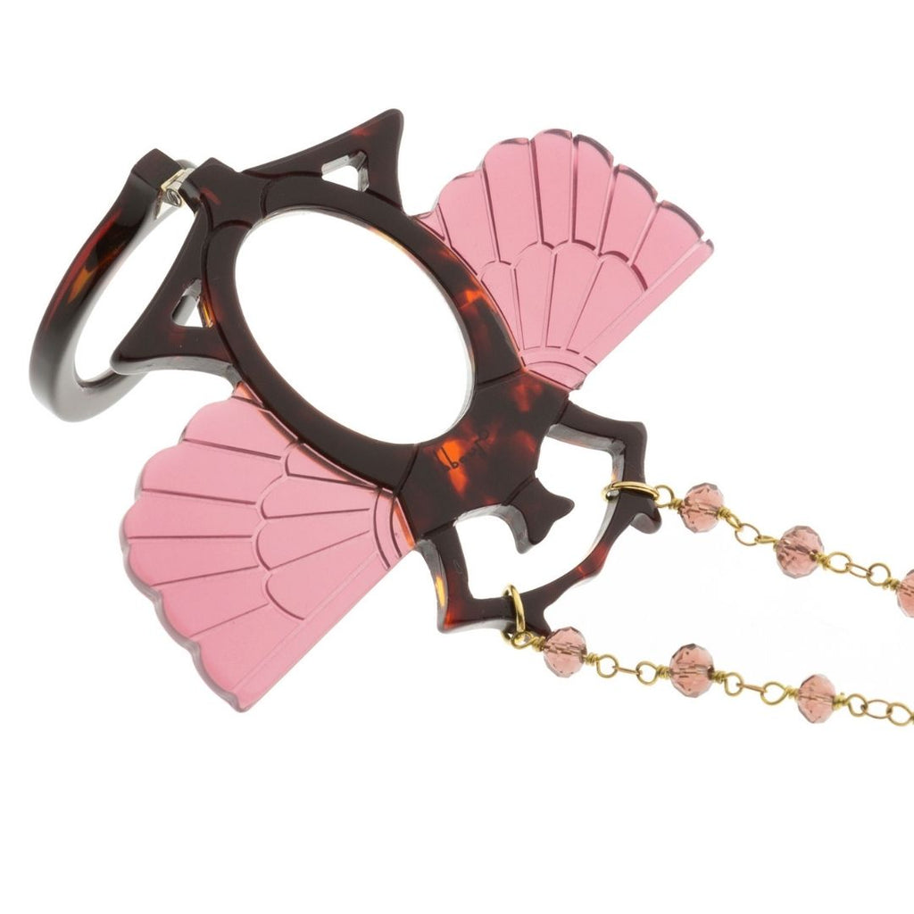 Colgante-gafas en forma de escarabajo egipcio. Realizado en combinación de acetato imitación carey con las alas en rosa transparente. Cadena de rosario en latón con cuentas de vidrio rosa. Una bisagra hace que se pueda transformar en gafas de lectura