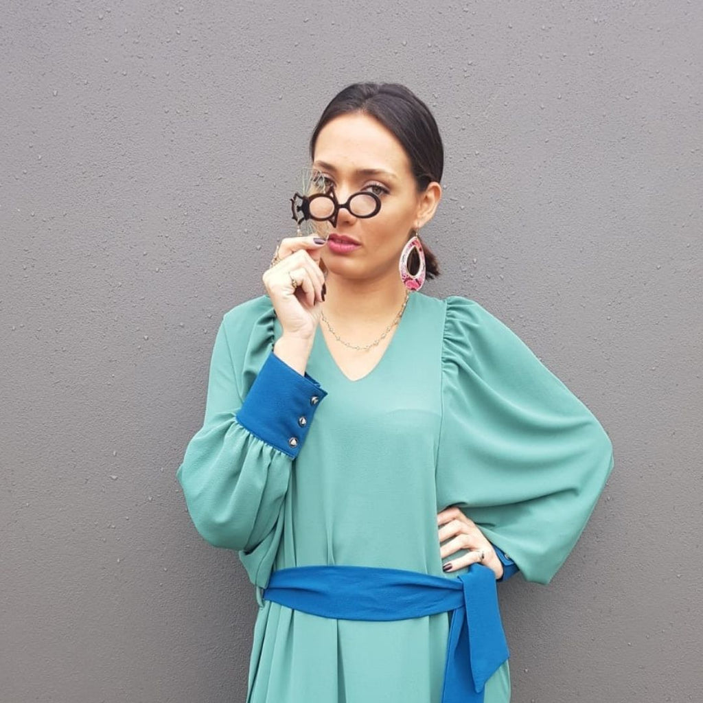 Mujer utilizando Colgante-gafas en forma de escarabajo egipcio. Realizado en combinación de acetato imitación carey con las alas en verde transparente. Cadena de rosario en latón con cuentas de vidrio azul. Una bisagra hace que se pueda transformar en gafas de lectura