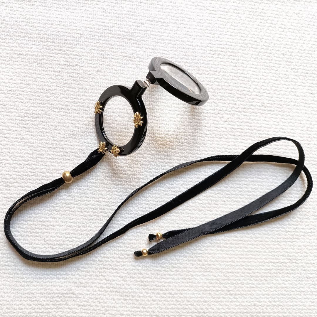Colgante gafas Hormigas, realizado en acetato color negro con hormigas metálicas doradas y collar de terciopelo negro con fornituras  y abalorios dorados. El colgante tiene una bisagra que hace que se pueda desplegar y transformar en gafas de lectura.
